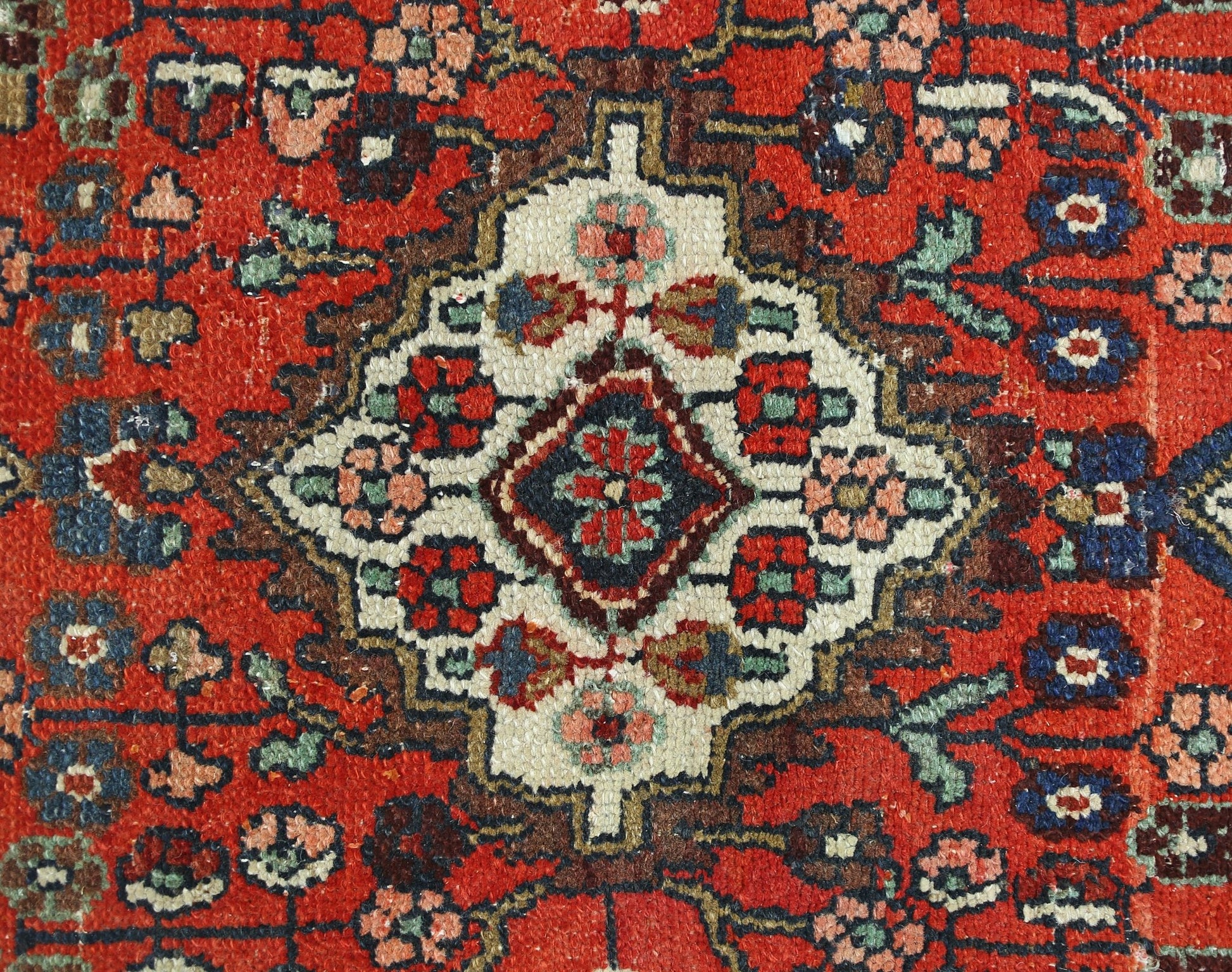A vintage Persian Sarouk rug featuring a central floral medallion on a vibrant red background.
