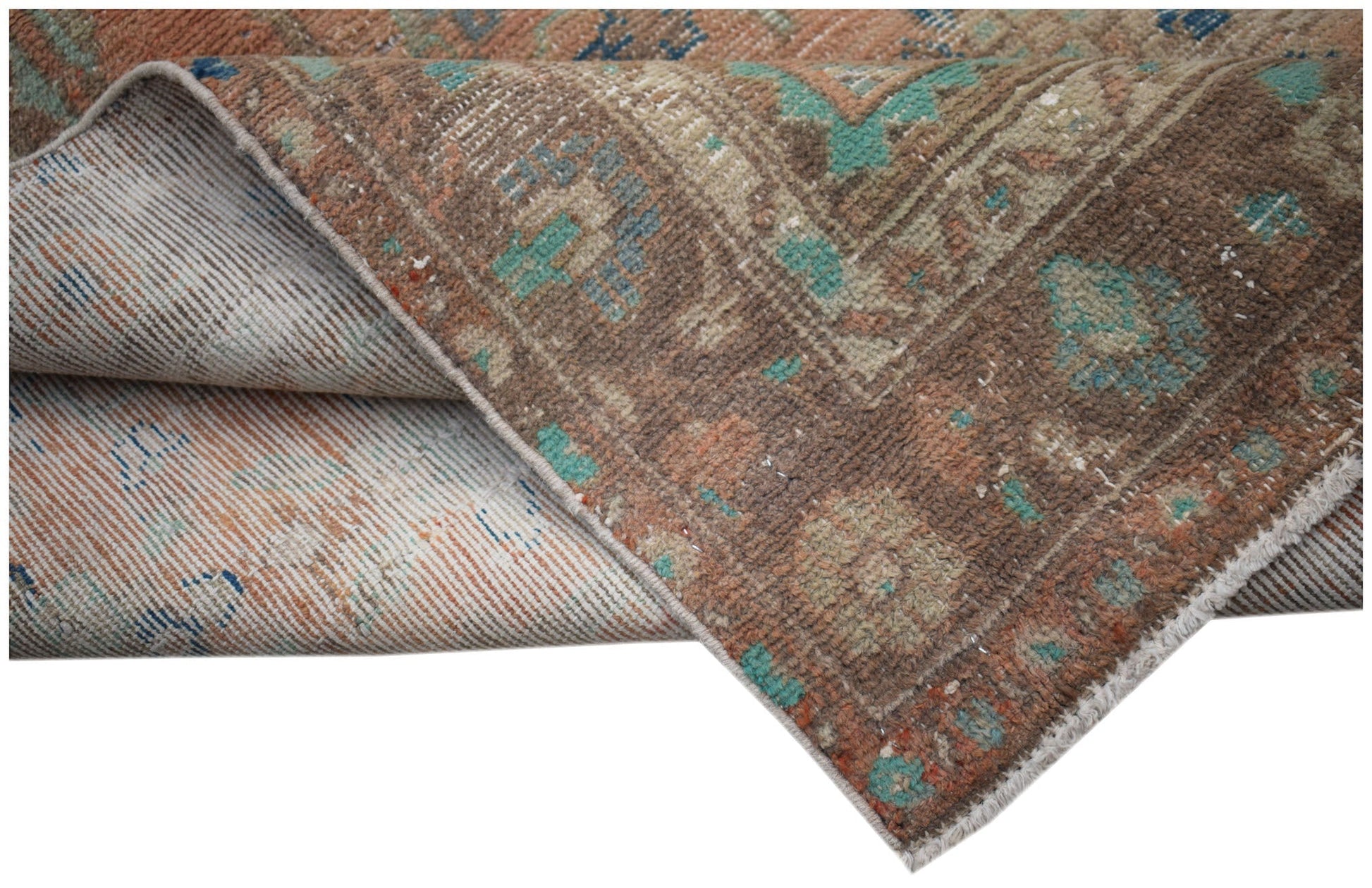 A vintage Persian Sarouk rug with a worn brown and teal floral pattern folded to show its backing.