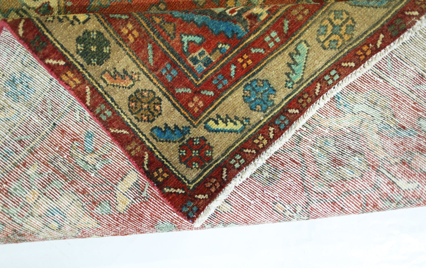 A folded vintage Persian Sarouk rug featuring intricate floral patterns in red, blue, and tan.