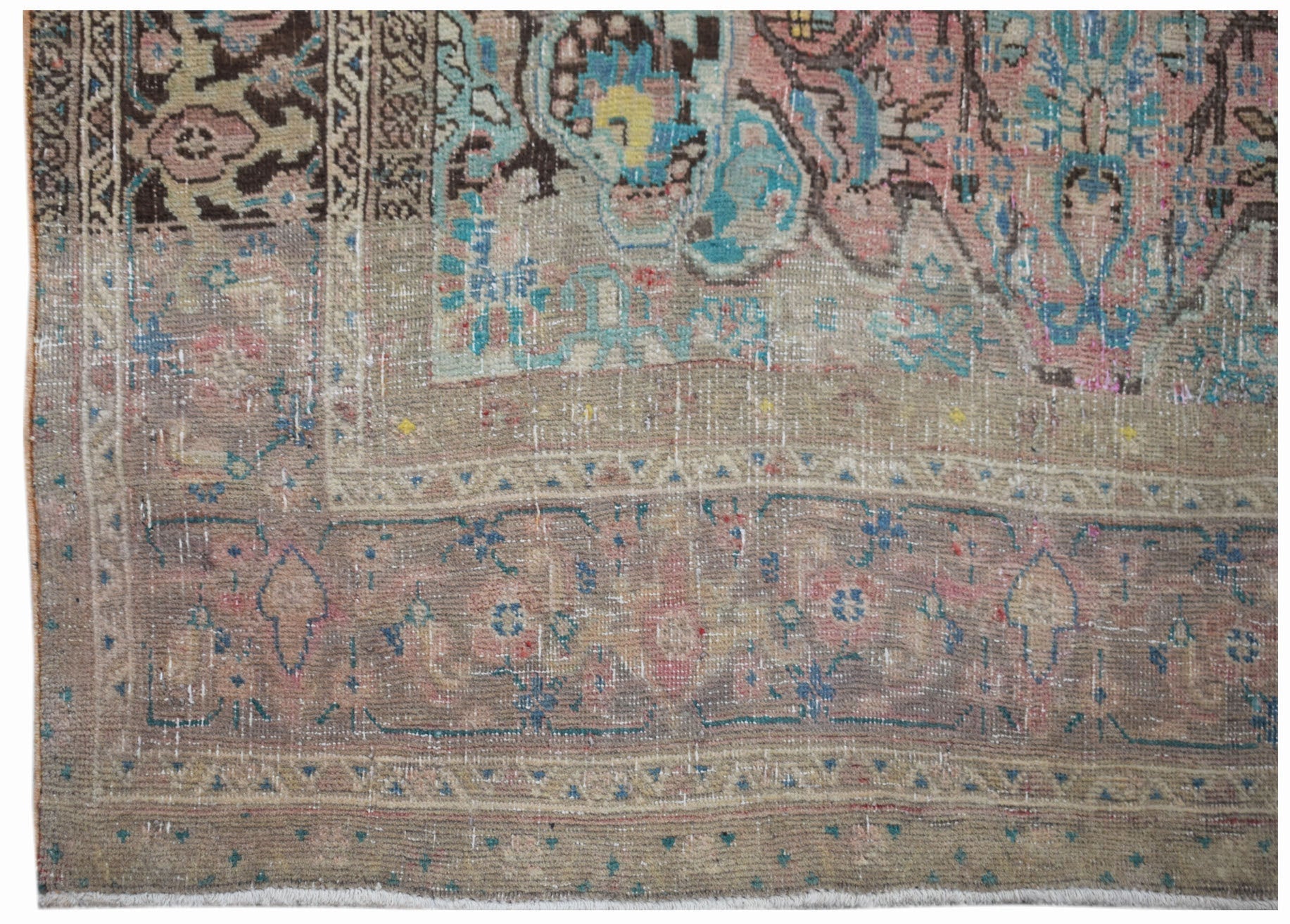 A handwoven vintage Persian rug featuring a faded floral pattern in muted pink, blue, and brown.