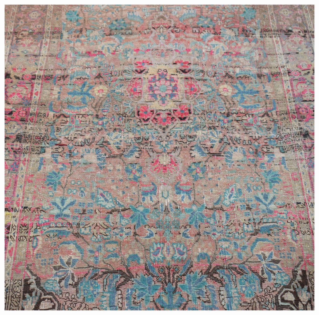 A vintage handwoven Persian rug featuring a faded floral pattern in shades of pink and blue.