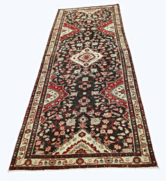 A vintage Persian Sarouk runner featuring a dark field with intricate red and cream floral patterns.
