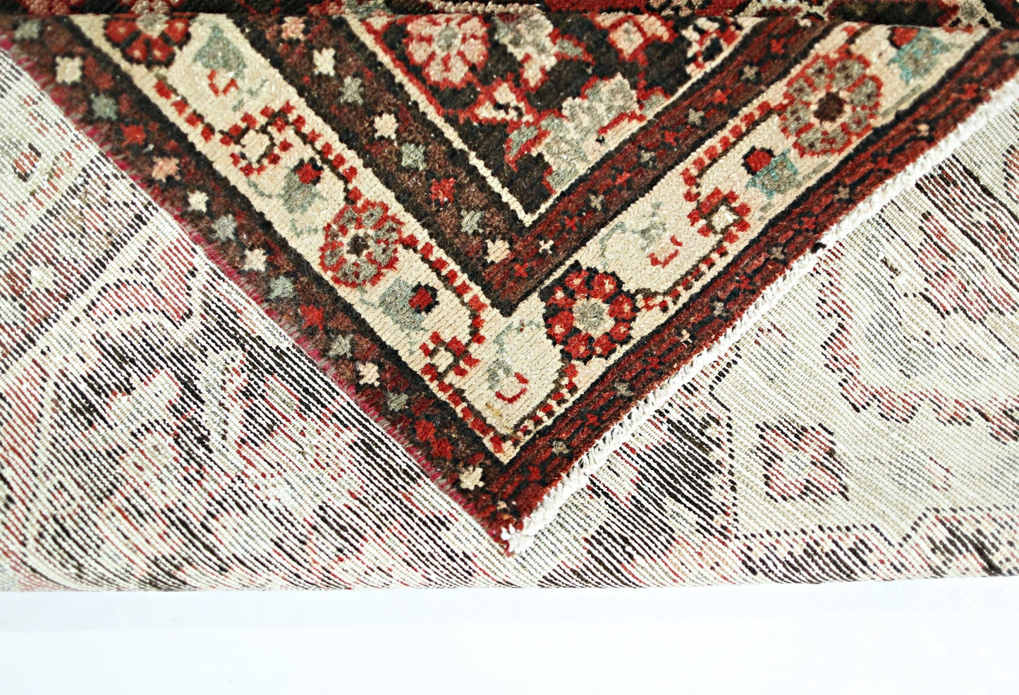 A corner of a vintage Persian Sarouk runner showing its intricate floral pattern and wool weave.