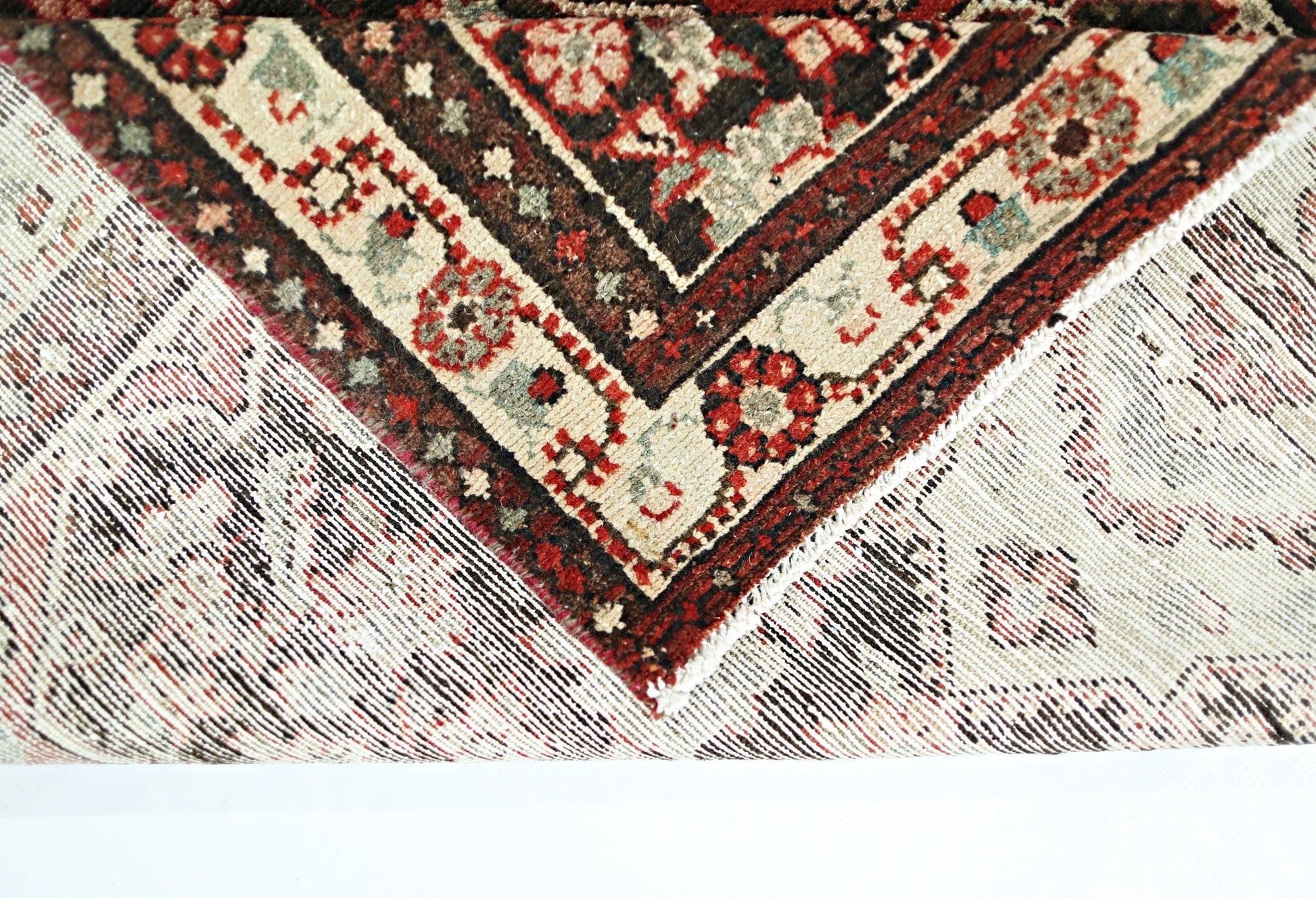 A corner of a vintage Persian Sarouk runner showing its intricate floral pattern and wool weave.