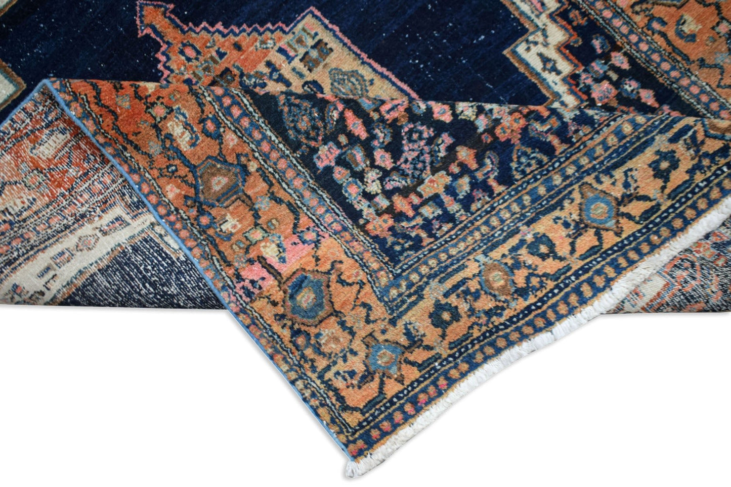 A handwoven vintage Persian rug featuring a dark blue field with orange and pink floral patterns.