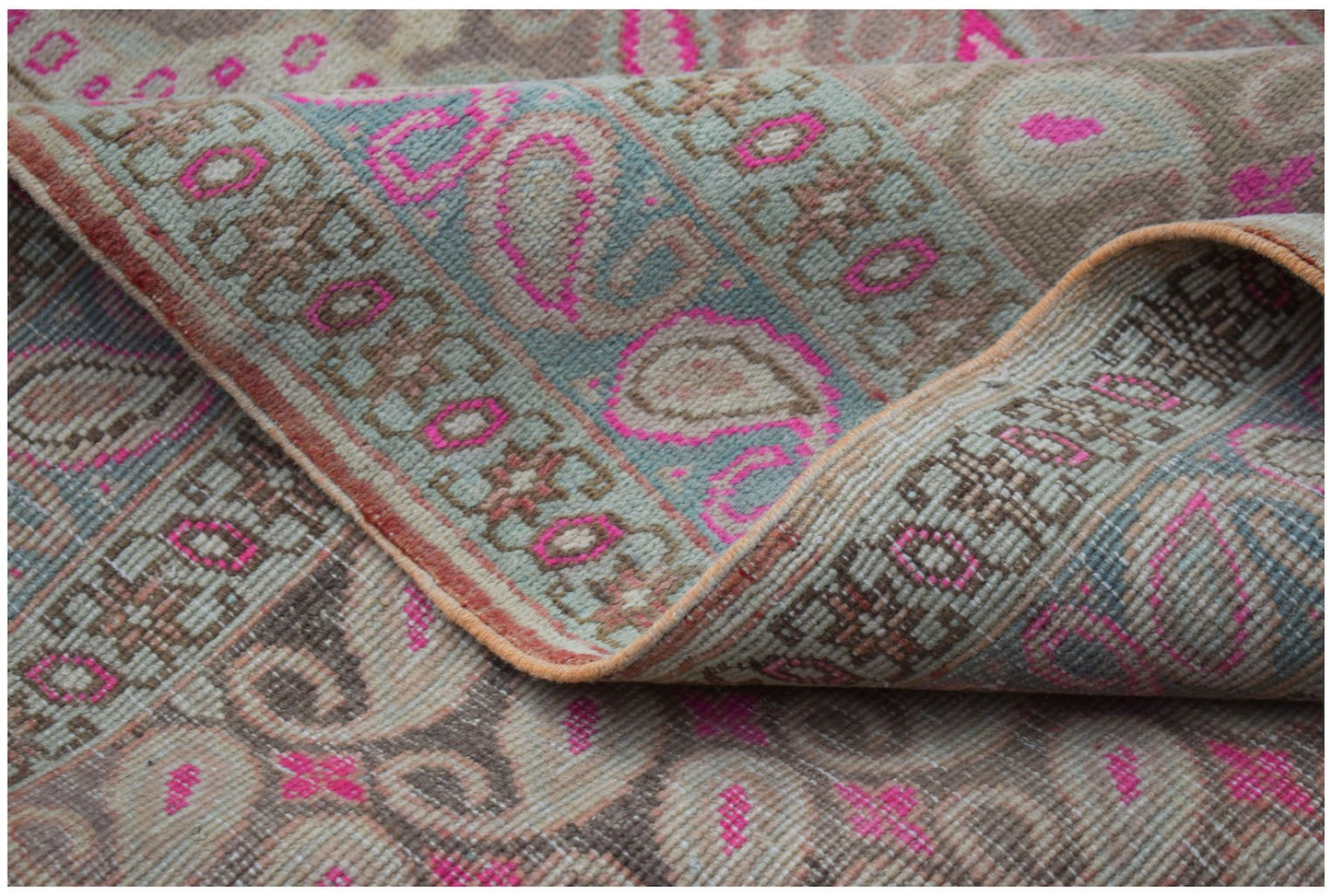 A vintage Persian Senneh rug featuring a faded paisley pattern with vibrant pink accents.