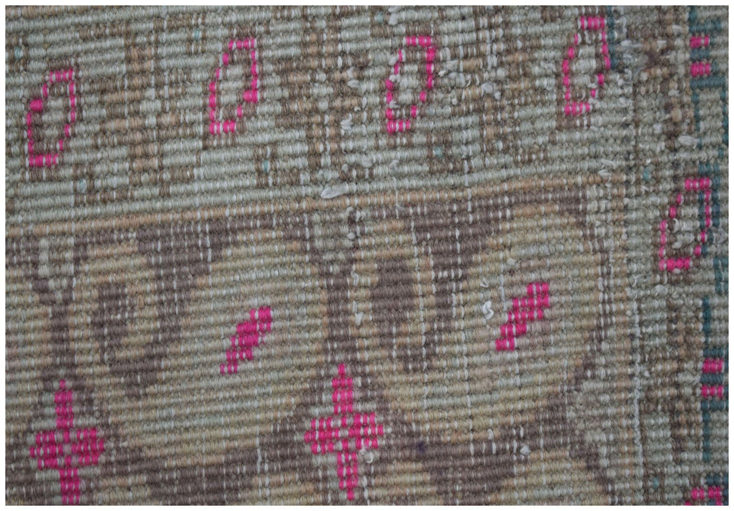 A close-up of a vintage Persian Senneh rug featuring a worn texture and pink geometric accents.