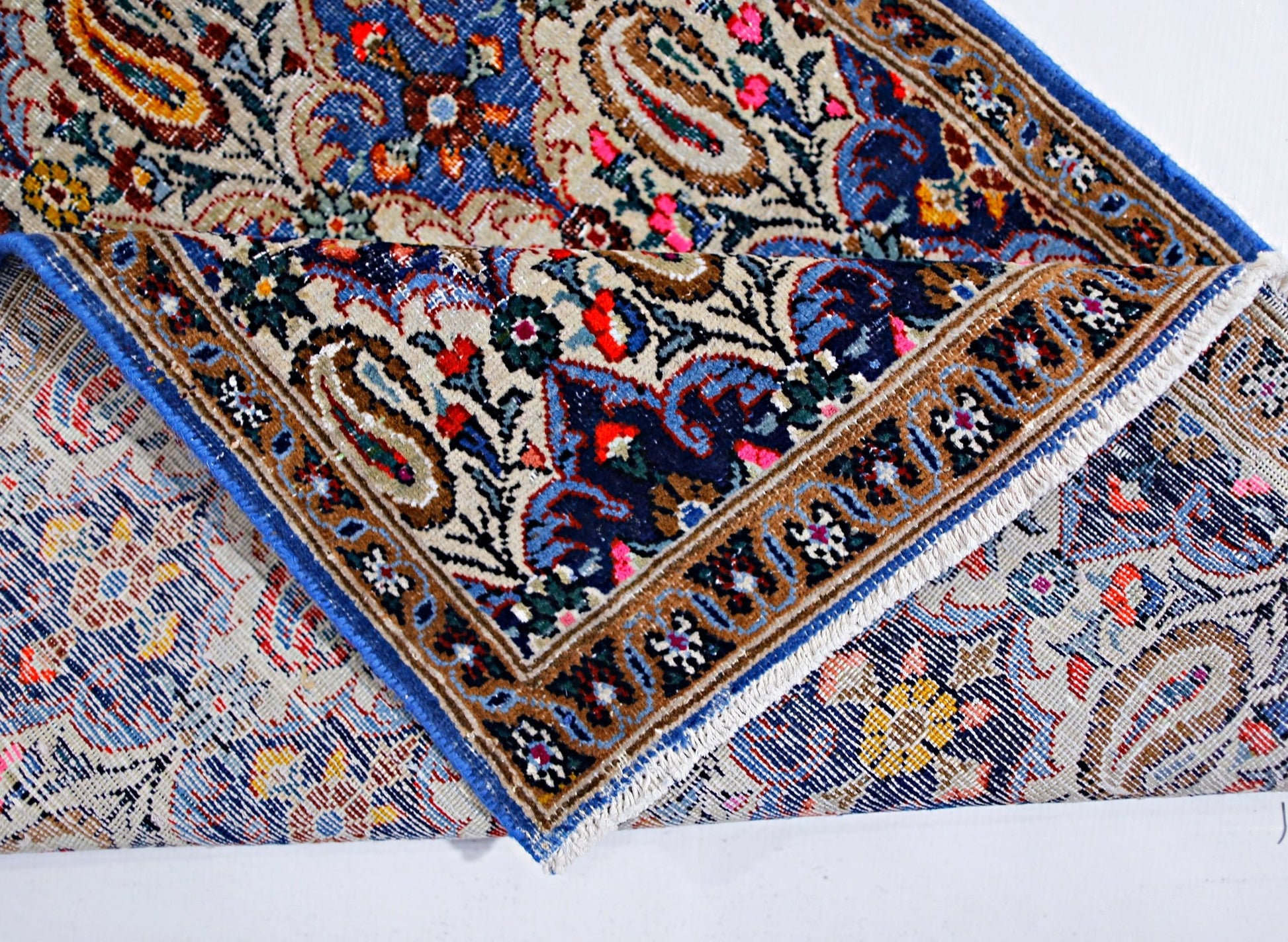 A vintage Persian Senneh runner with a folded corner revealing its intricate floral and paisley pattern.