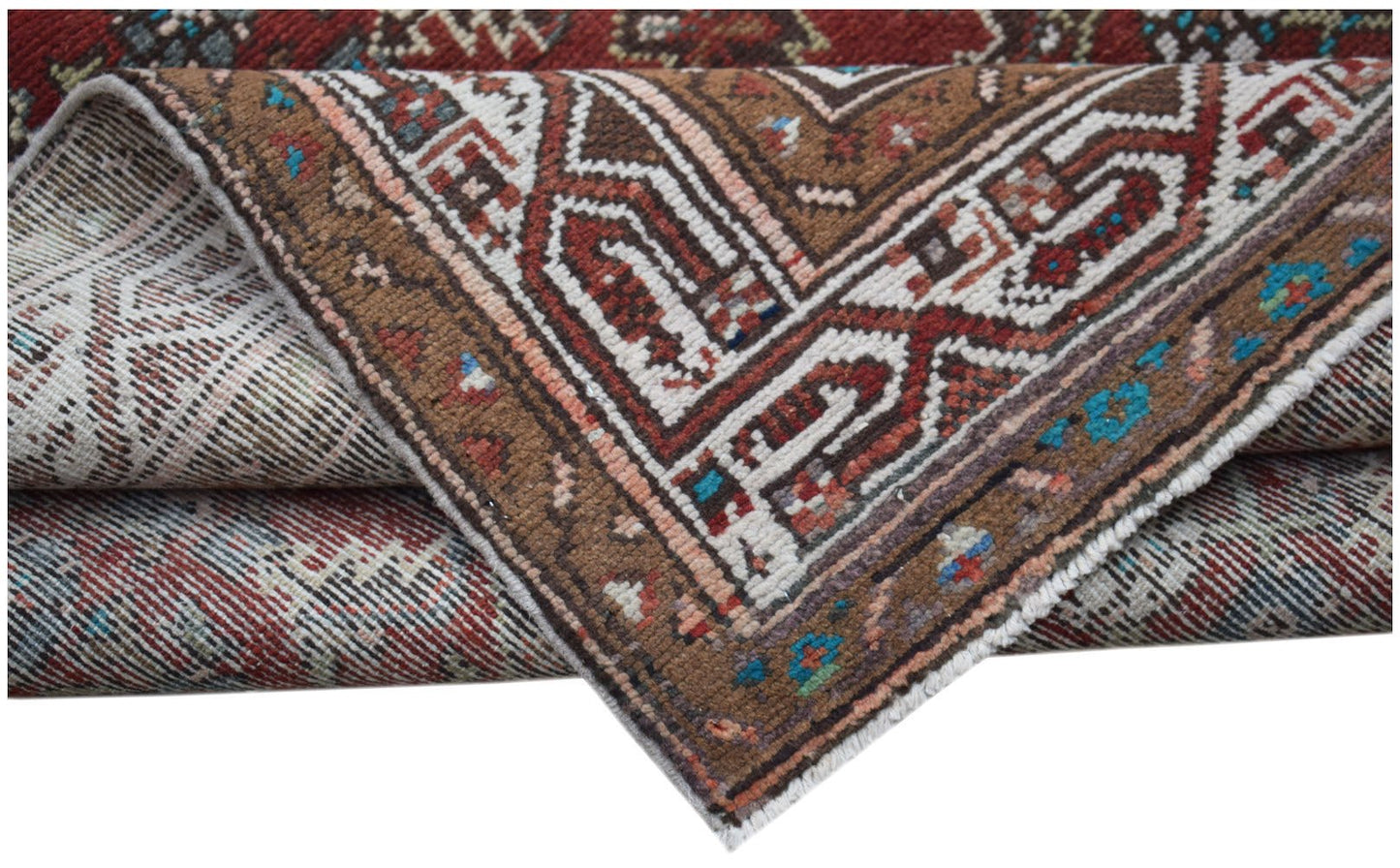 A folded vintage Persian Senneh runner featuring intricate geometric patterns in red and brown.
