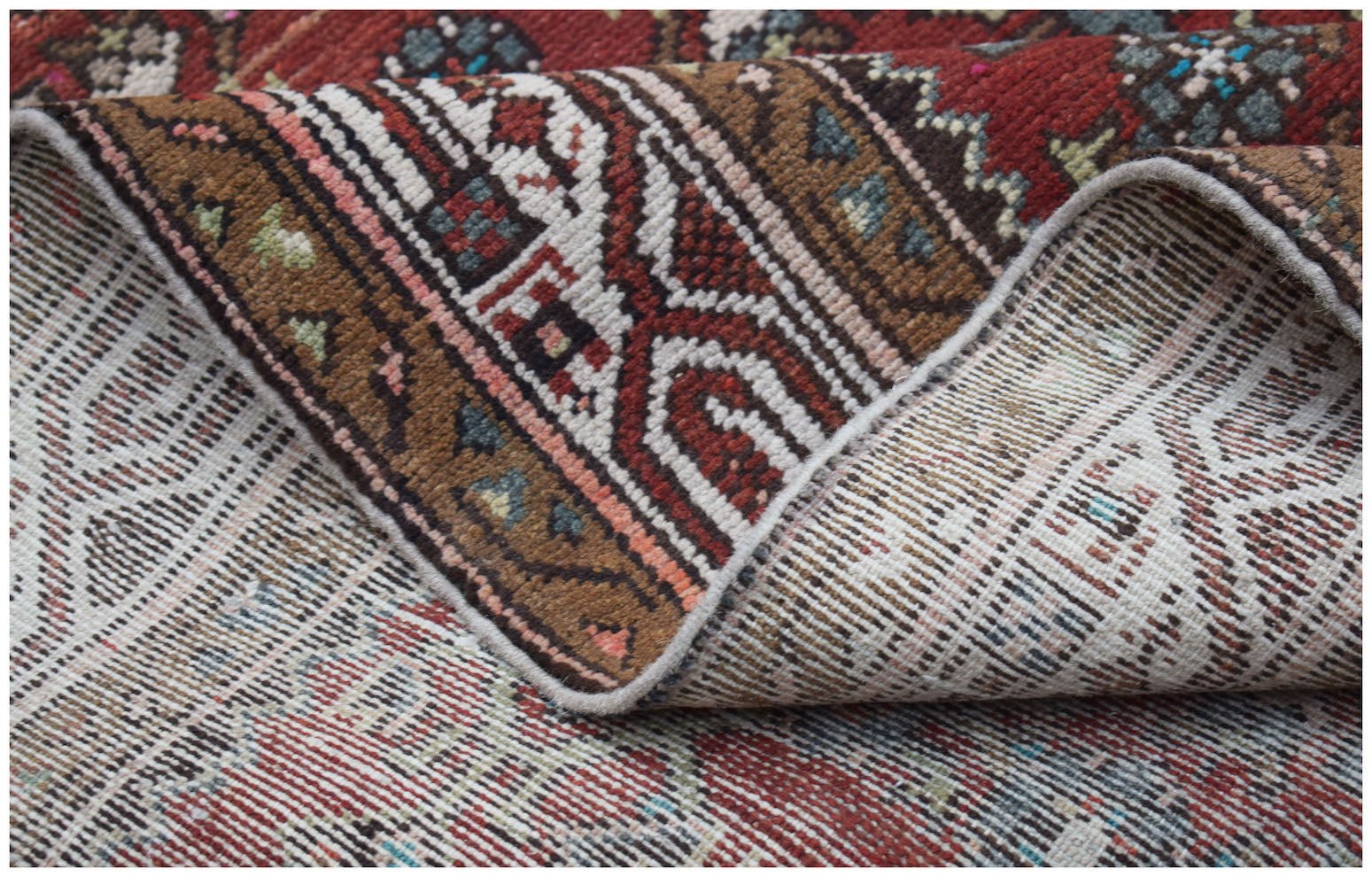 A corner of a vintage Persian Senneh runner is folded back to show its handwoven wool construction.