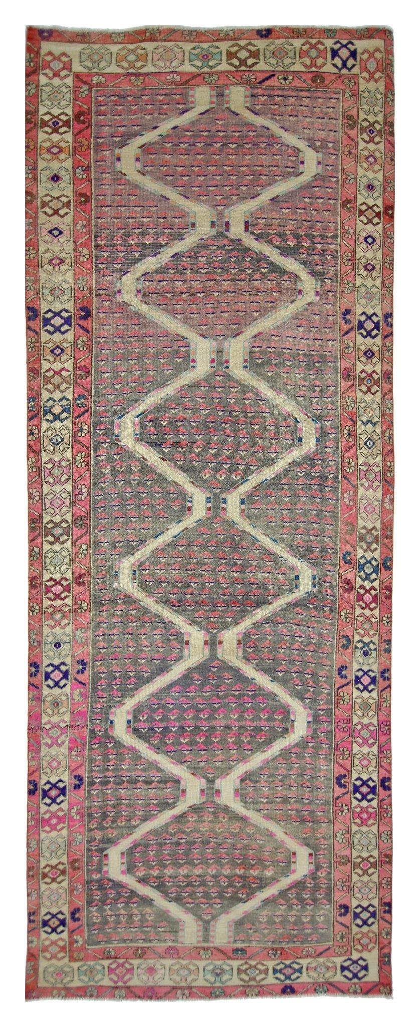 A vintage Persian Senneh runner featuring a repeating diamond pattern in pink and grey tones.