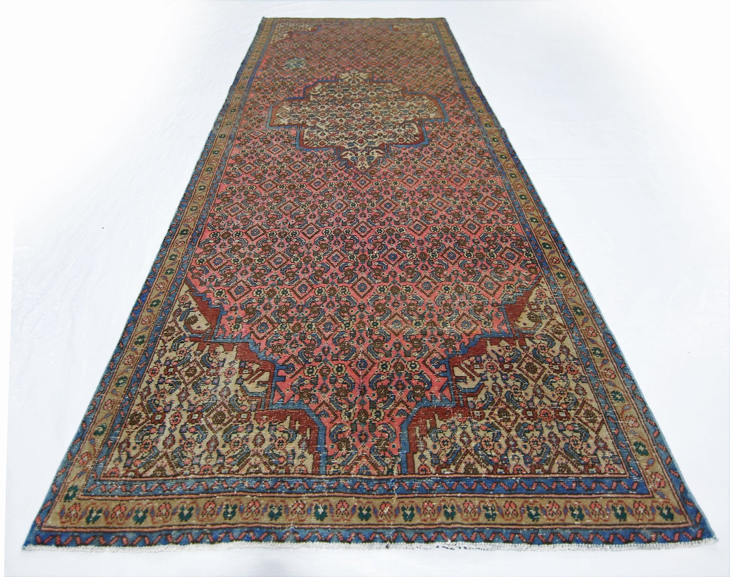 A vintage Persian Senneh runner featuring a geometric pattern in red, blue, and beige tones.