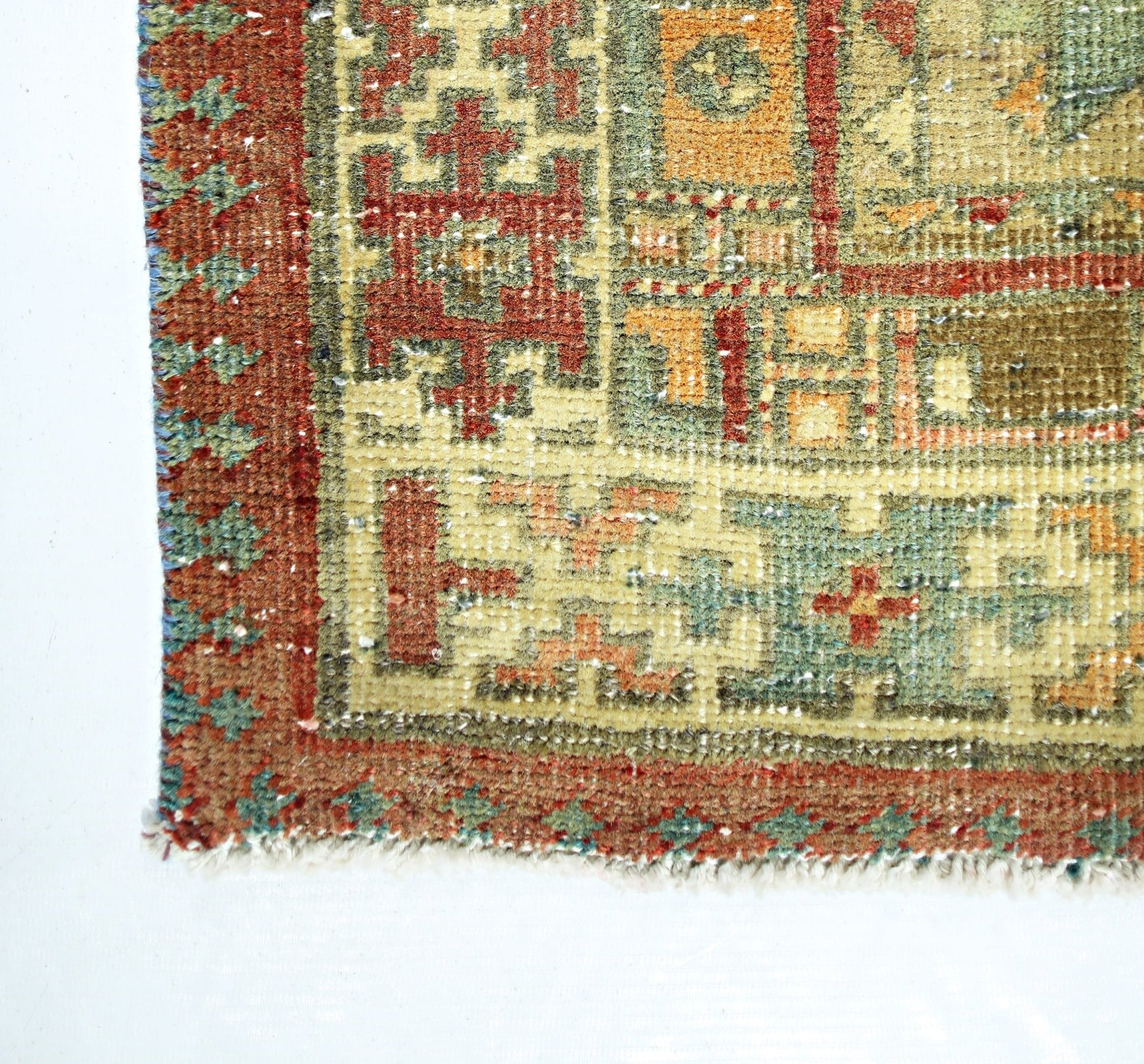 A close-up of a vintage Persian rug featuring geometric patterns in red, green, and orange tones.