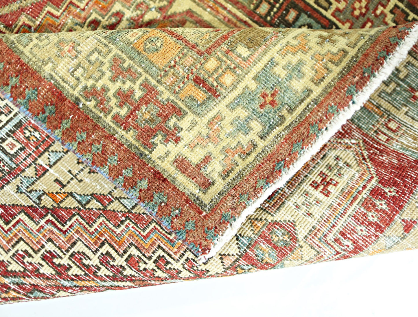 A folded vintage Persian rug featuring intricate geometric patterns in red, green, and tan wool.