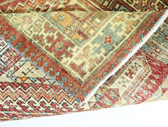 A folded vintage Persian rug featuring intricate geometric patterns in red, green, and tan wool.