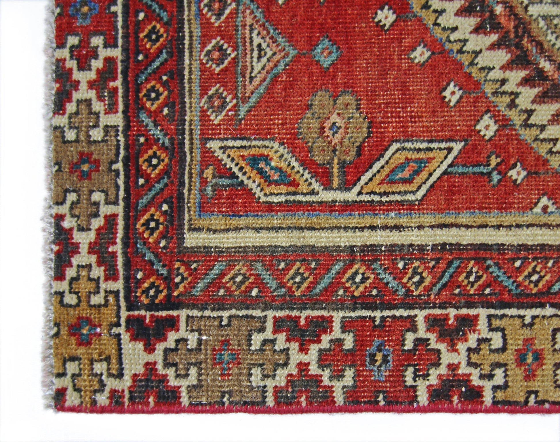 A close-up of a vintage Persian Serab runner featuring geometric patterns in red, blue, and tan.