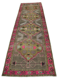 A vintage Persian Serab runner rug featuring geometric patterns in olive, grey, and vibrant pink.
