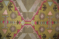 A vintage Persian Serab runner featuring geometric tribal patterns in olive, pink, and brown tones.