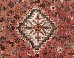 A vintage handwoven Persian Shiraz rug featuring a central white diamond motif on a red field.