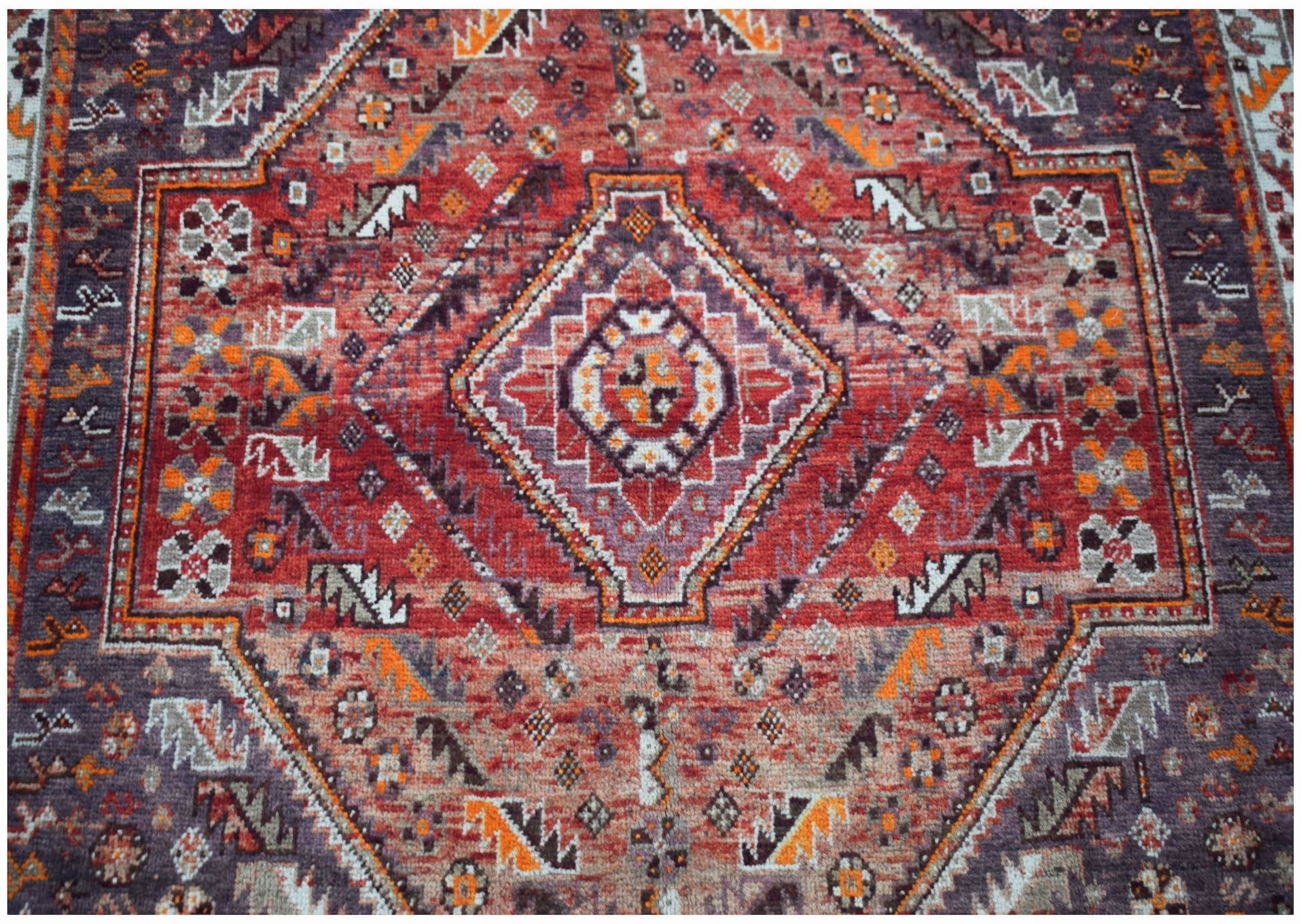 A vintage handwoven Persian Shiraz rug featuring a geometric diamond pattern in red and purple.