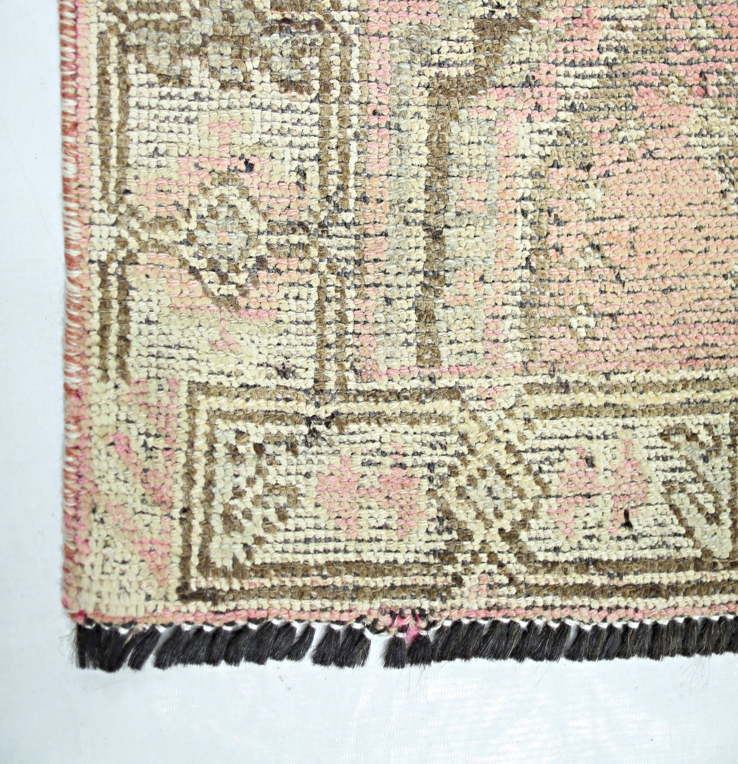 A vintage Persian Shiraz rug featuring a faded geometric pattern in pink and beige with dark fringe.