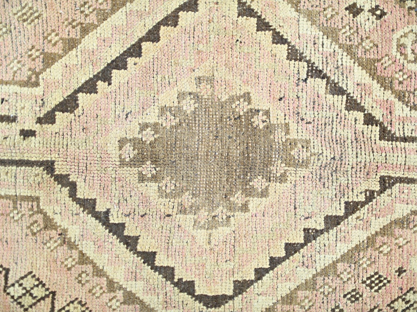 A vintage Persian Shiraz rug featuring a central brown diamond medallion on a soft pink background.