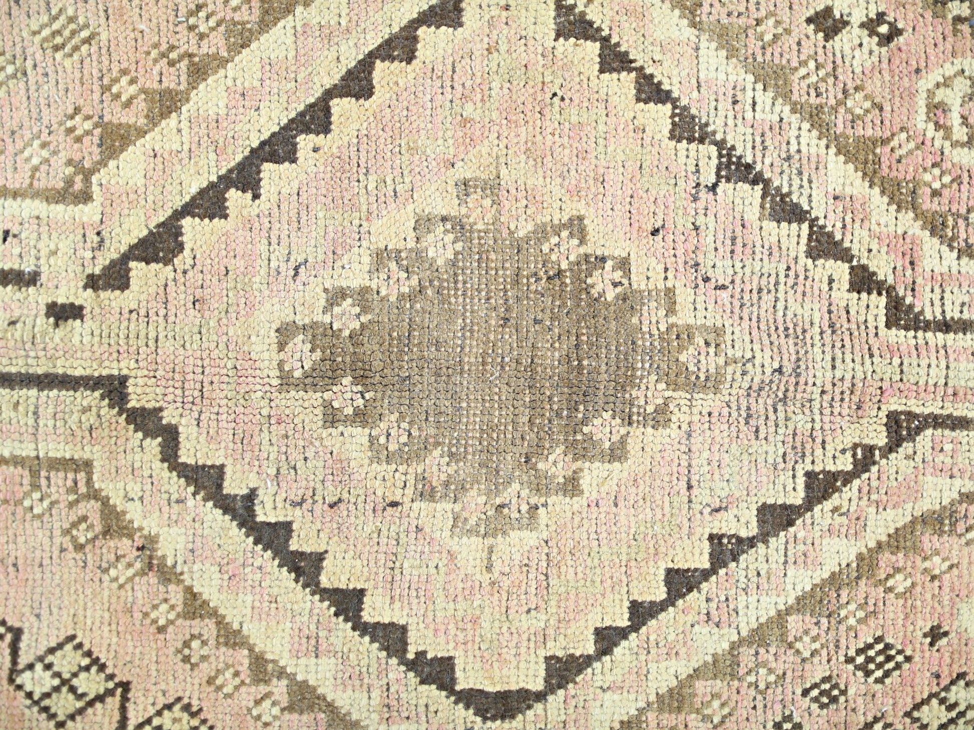 A vintage Persian Shiraz rug featuring a central brown diamond medallion on a soft pink background.