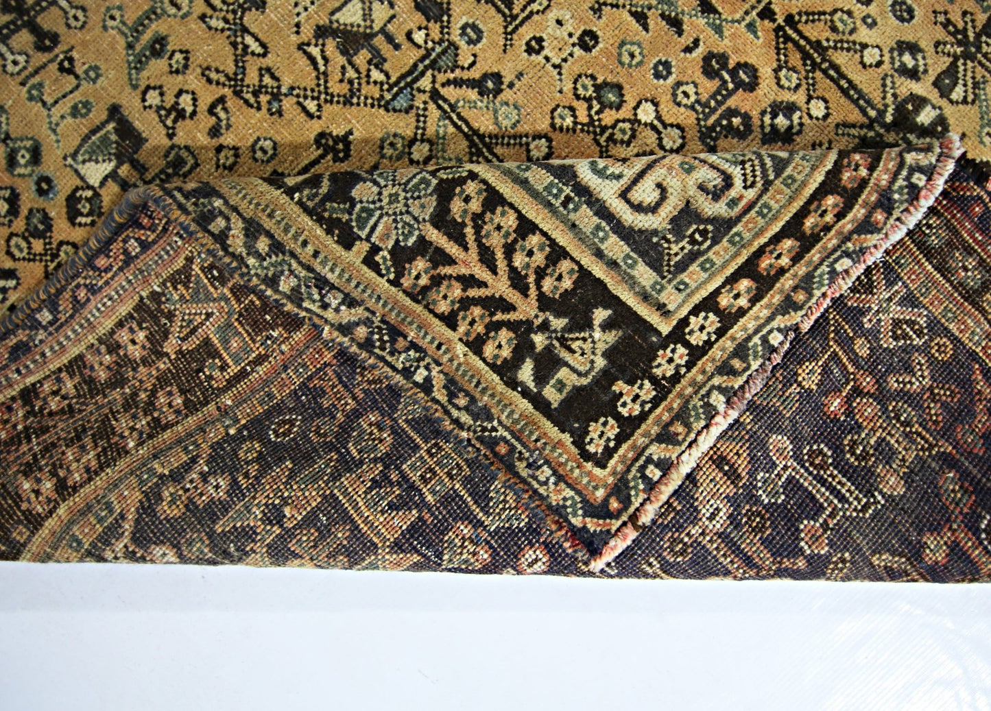 A corner of a vintage Persian Shiraz rug is folded back to reveal its intricate wool pattern.