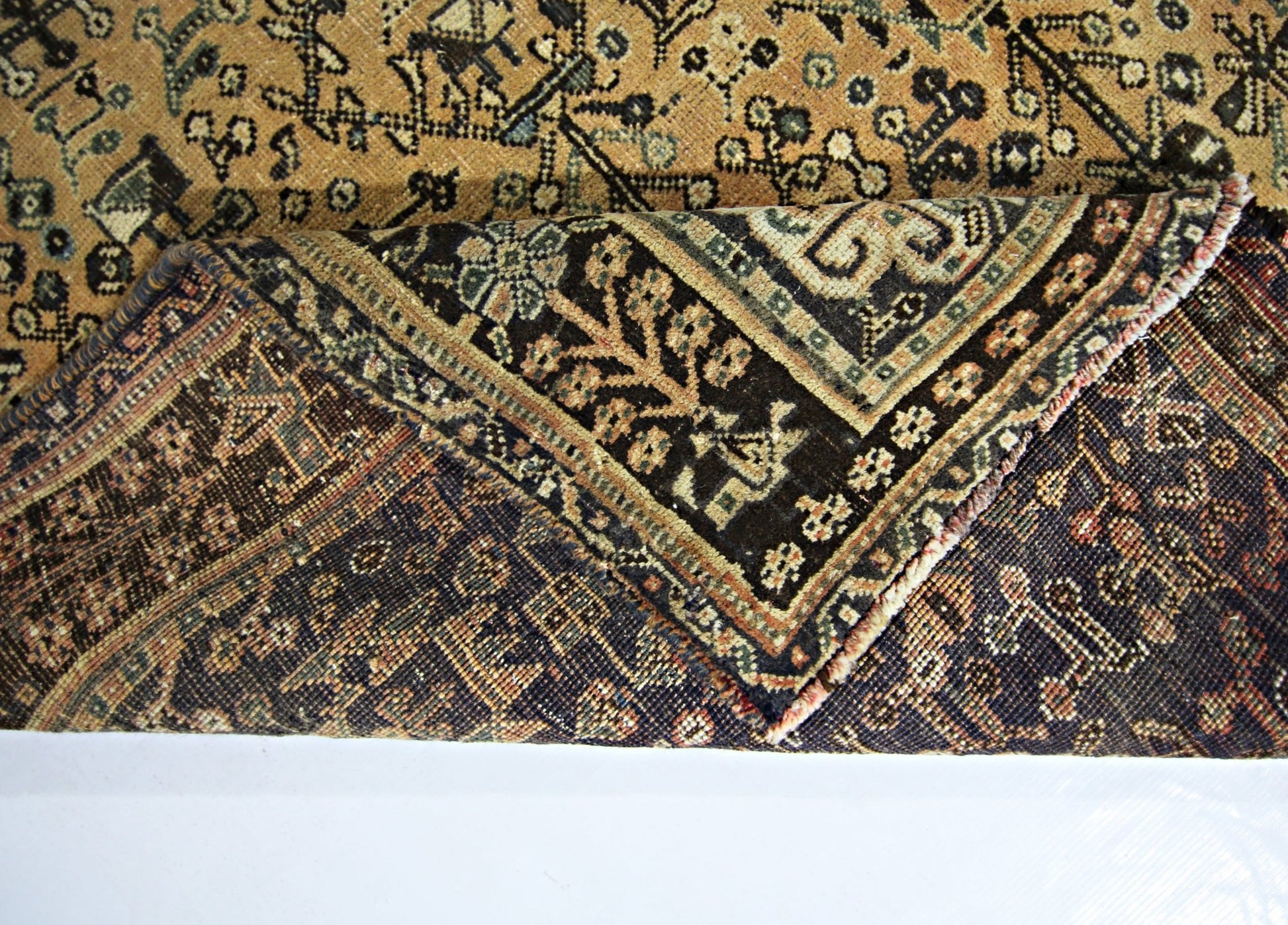 A corner of a vintage Persian Shiraz rug is folded back to reveal its intricate wool pattern.