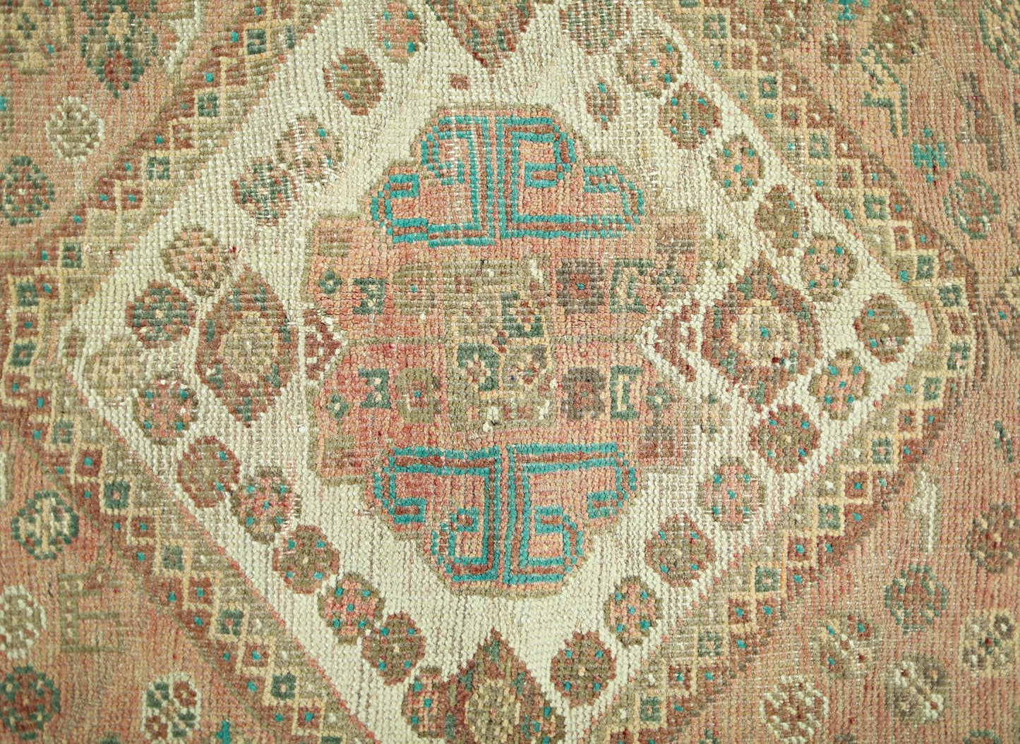 A vintage Persian Shiraz rug featuring a central geometric medallion in muted pink and teal tones.