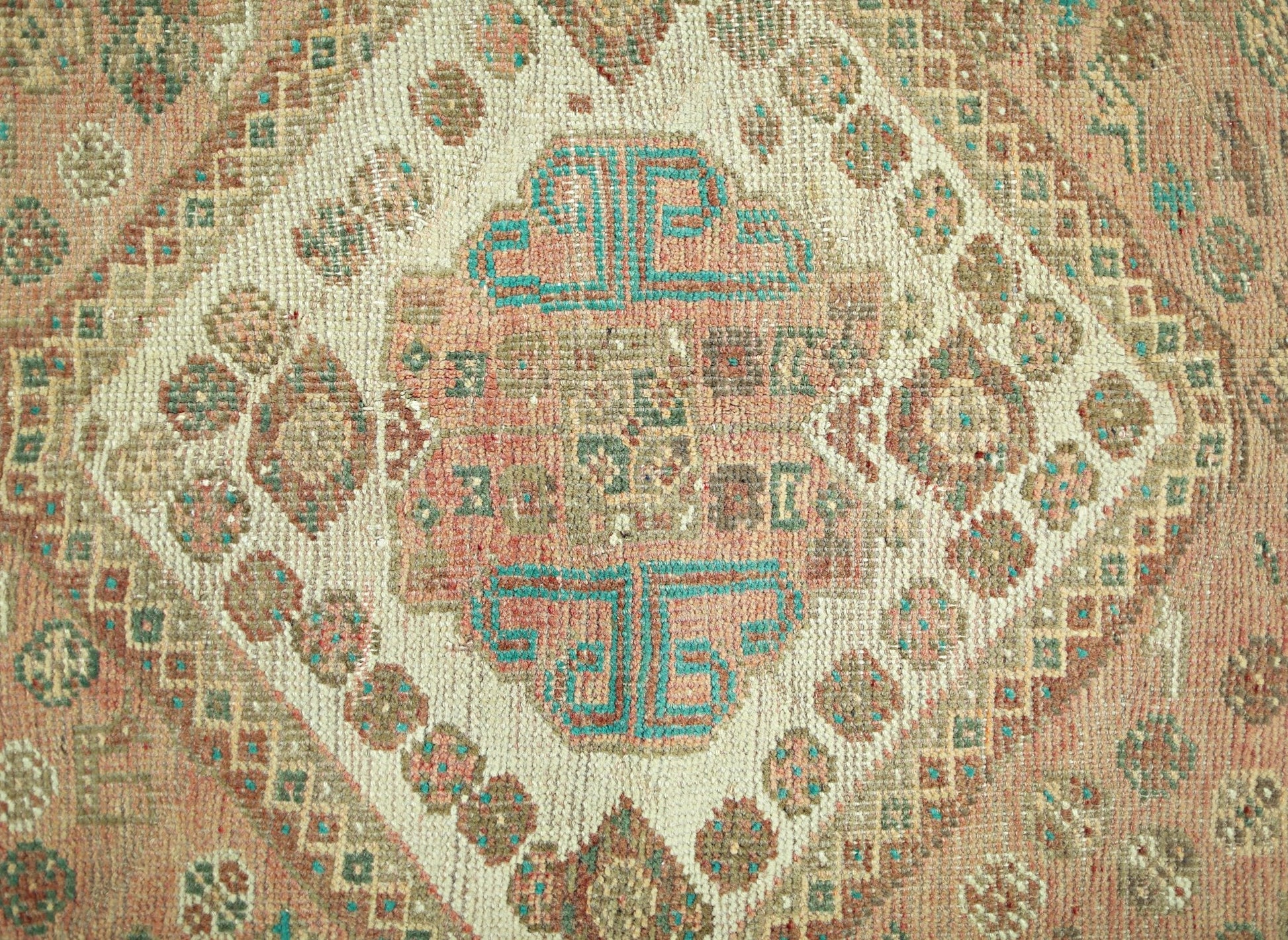 A vintage Persian Shiraz rug featuring a central geometric medallion in muted pink and teal tones.