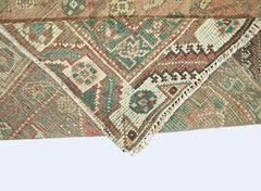 A folded vintage Persian Shiraz rug featuring intricate geometric patterns in muted earth tones.