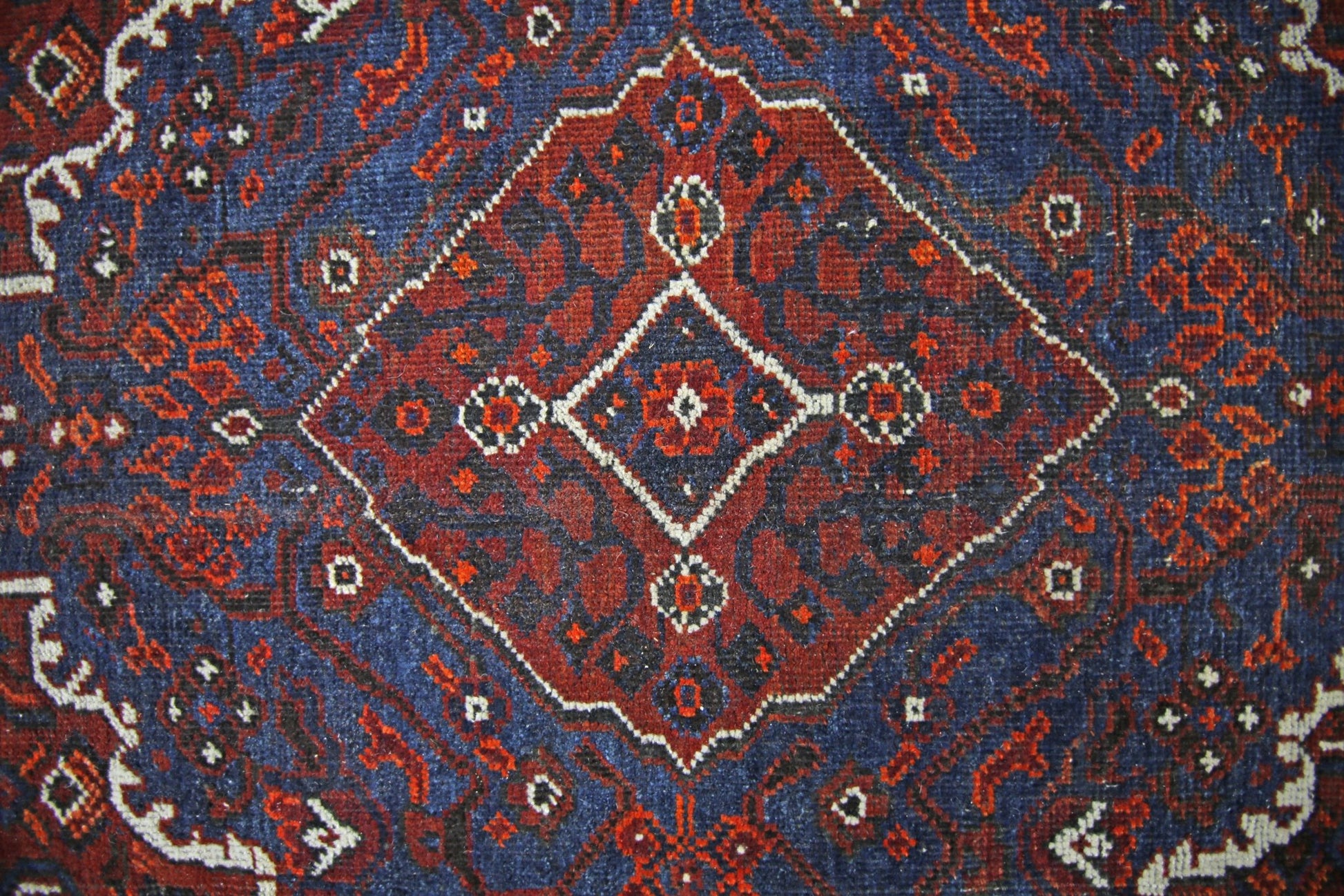 A vintage Persian Shiraz rug featuring a central diamond medallion in red and blue wool.