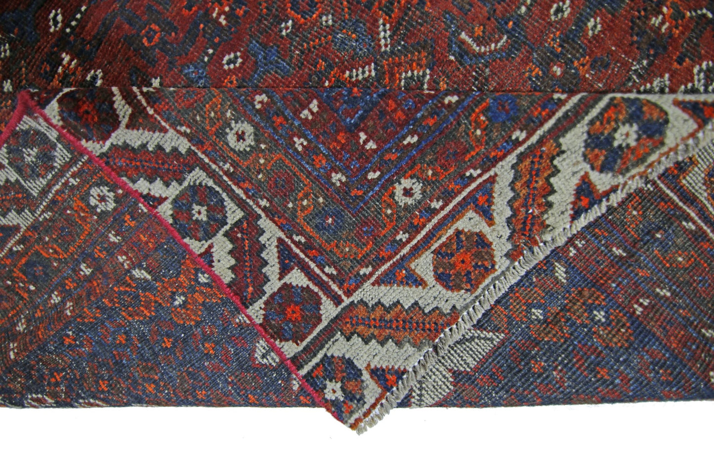 A corner of a vintage Persian Shiraz rug with a geometric pattern in red, blue, and cream.