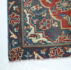 A corner view of a handmade vintage Persian rug featuring intricate floral patterns in red and blue.
