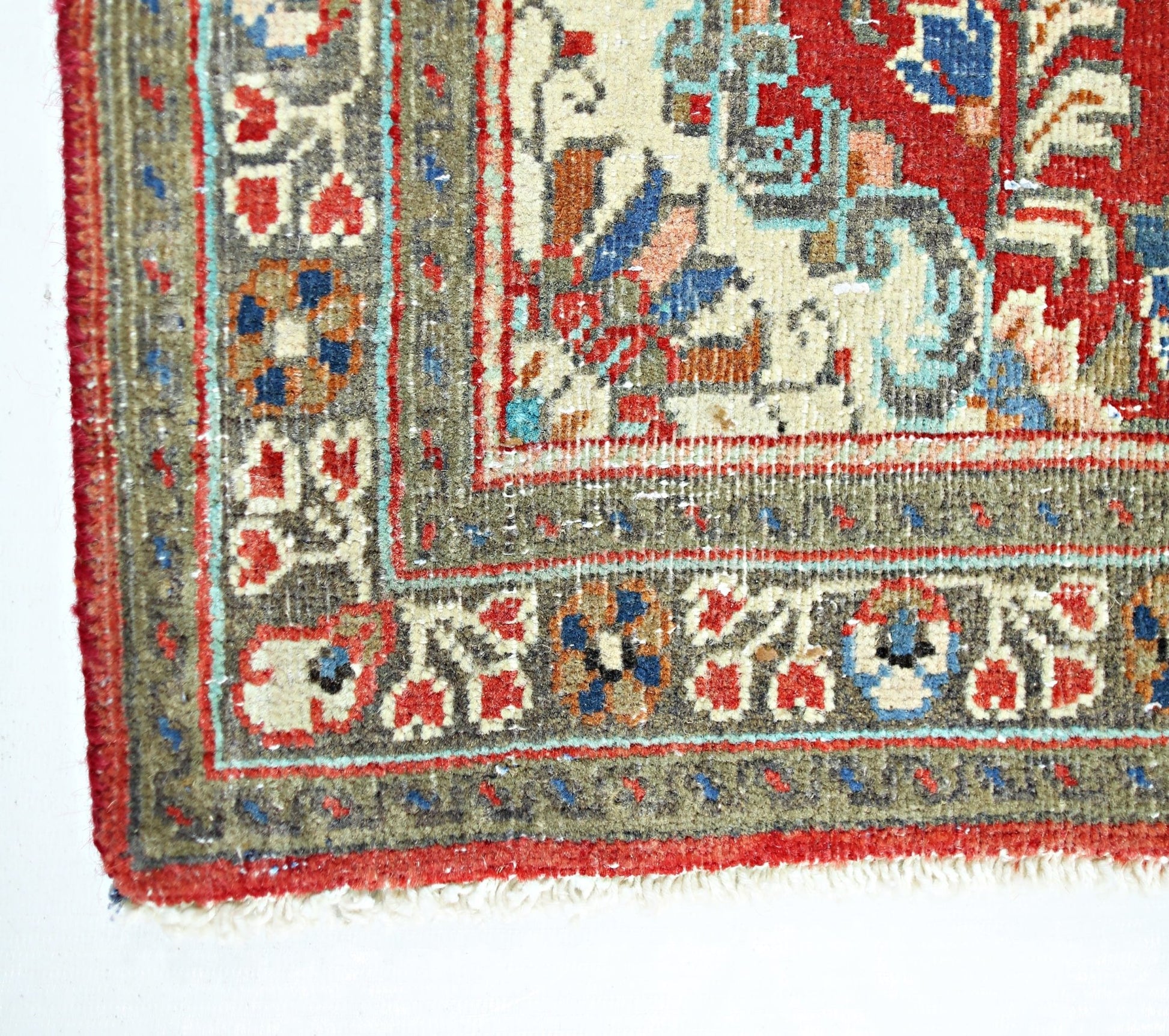 A corner view of a vintage Persian Tabriz rug featuring intricate floral patterns in red and blue.