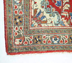 A corner view of a vintage Persian Tabriz rug featuring intricate floral patterns in red and blue.