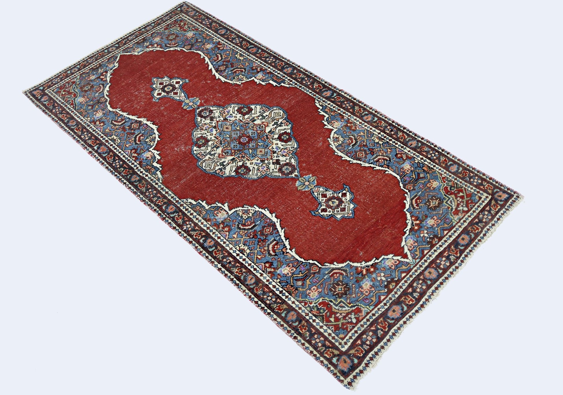 A vintage Persian rug featuring a central medallion on a red field with blue floral borders.