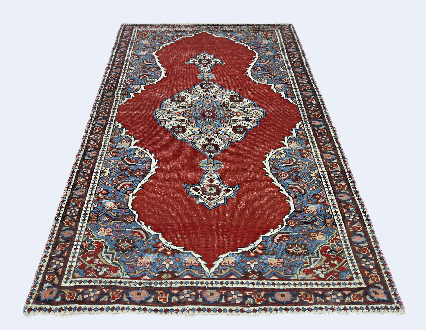 A handmade vintage Persian rug featuring a central medallion on a red field with blue floral borders.