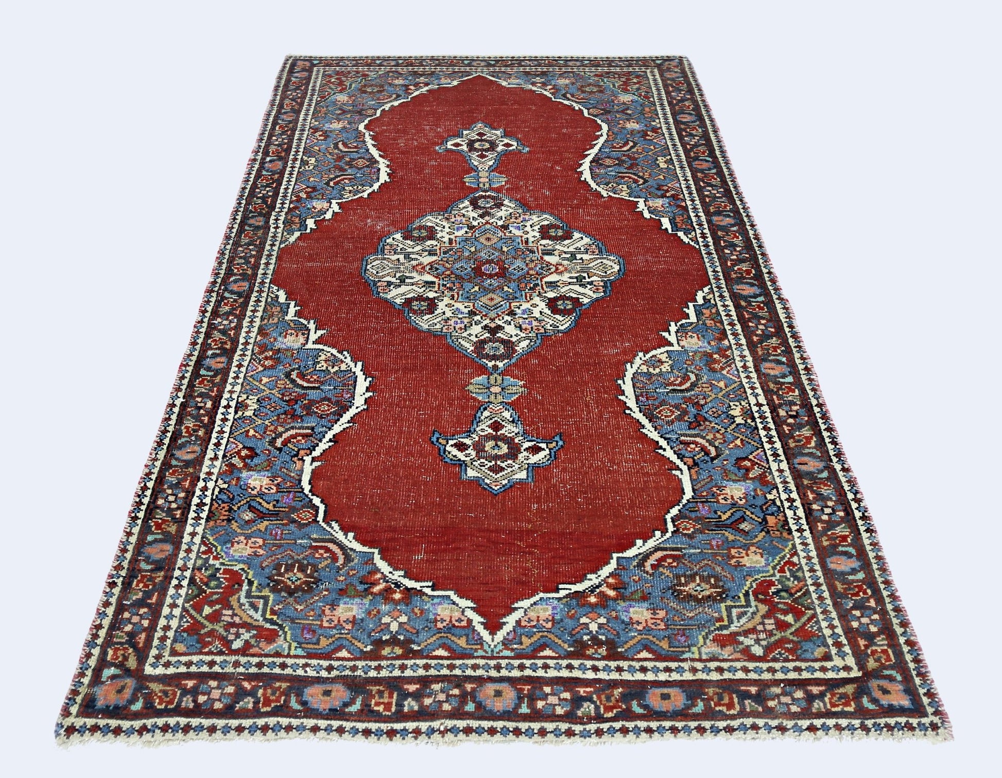 A handmade vintage Persian rug featuring a central medallion on a red field with blue floral borders.