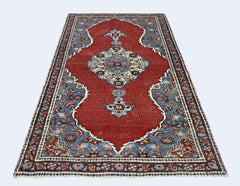 A handmade vintage Persian rug featuring a central medallion on a red field with blue floral borders.