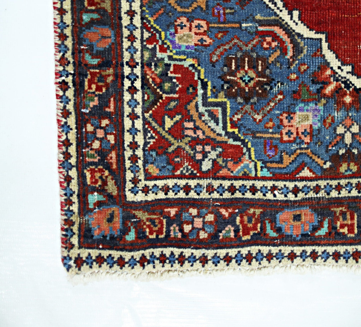 A corner view of a handmade vintage Persian rug featuring intricate floral patterns in red and blue.