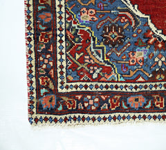 A corner view of a handmade vintage Persian rug featuring intricate floral patterns in red and blue.