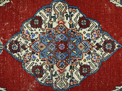A vintage Persian rug featuring a central blue and red floral medallion on a deep red background.