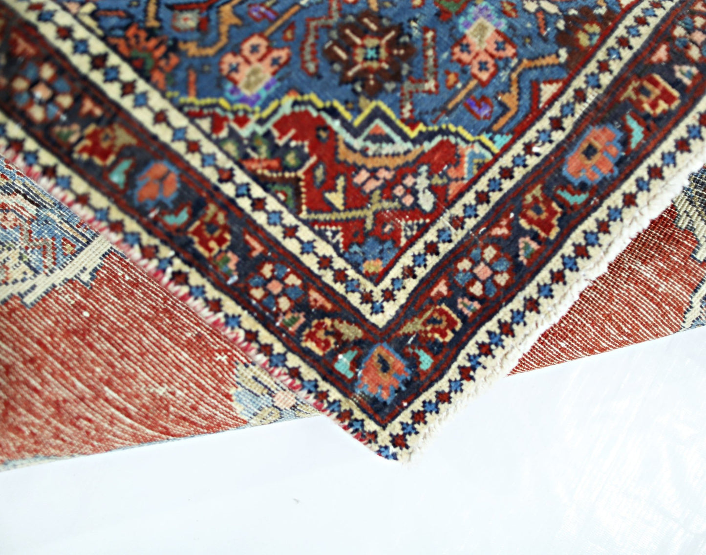 A folded vintage Persian rug featuring intricate geometric patterns in blue, red, and cream.