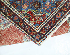 A folded vintage Persian rug featuring intricate geometric patterns in blue, red, and cream.