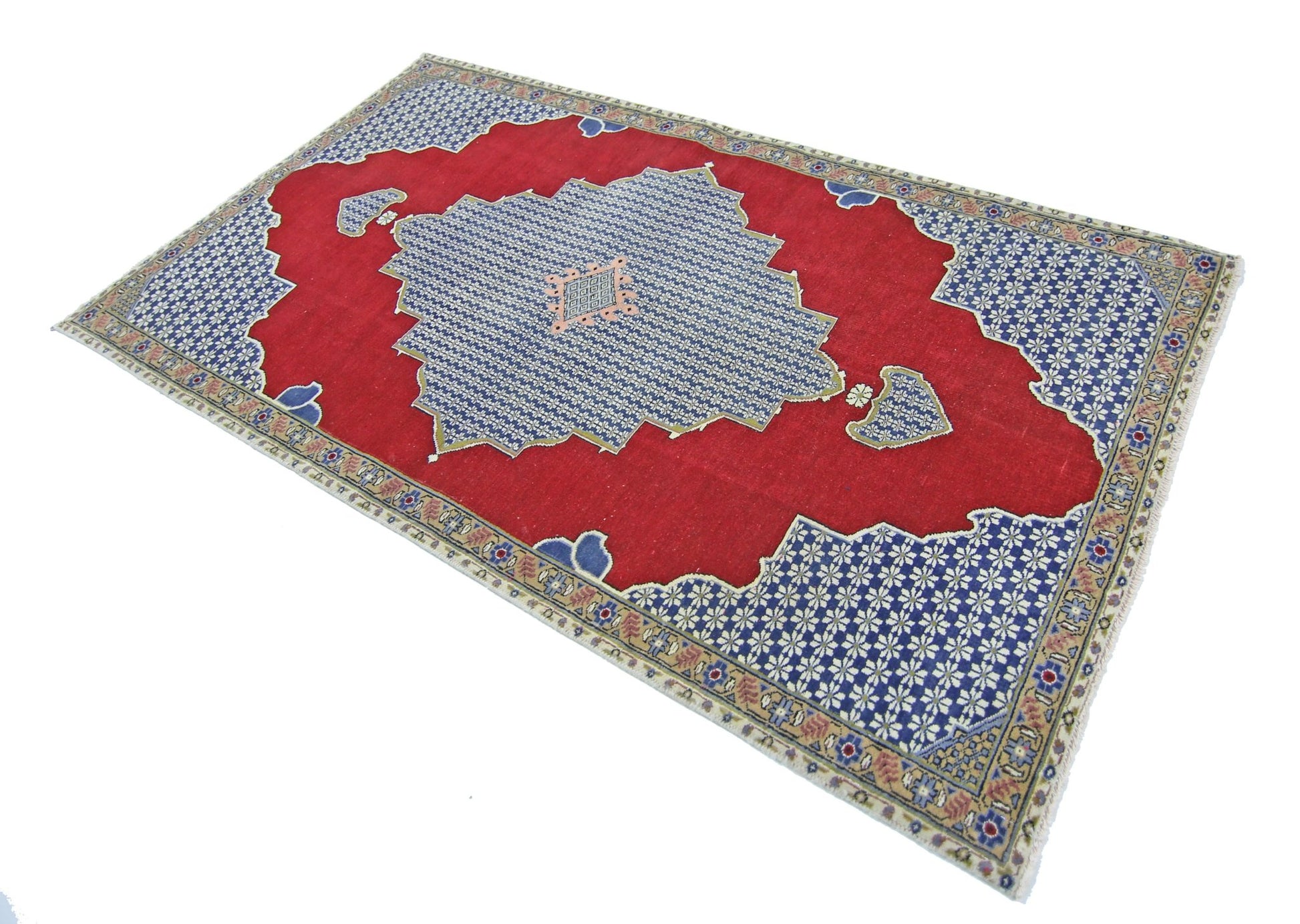 A vintage handmade Persian rug featuring a red field with a blue floral medallion and border.