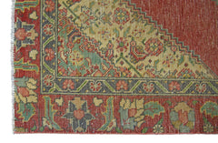 A corner view of a vintage Persian rug featuring intricate floral patterns in red, green, and cream.