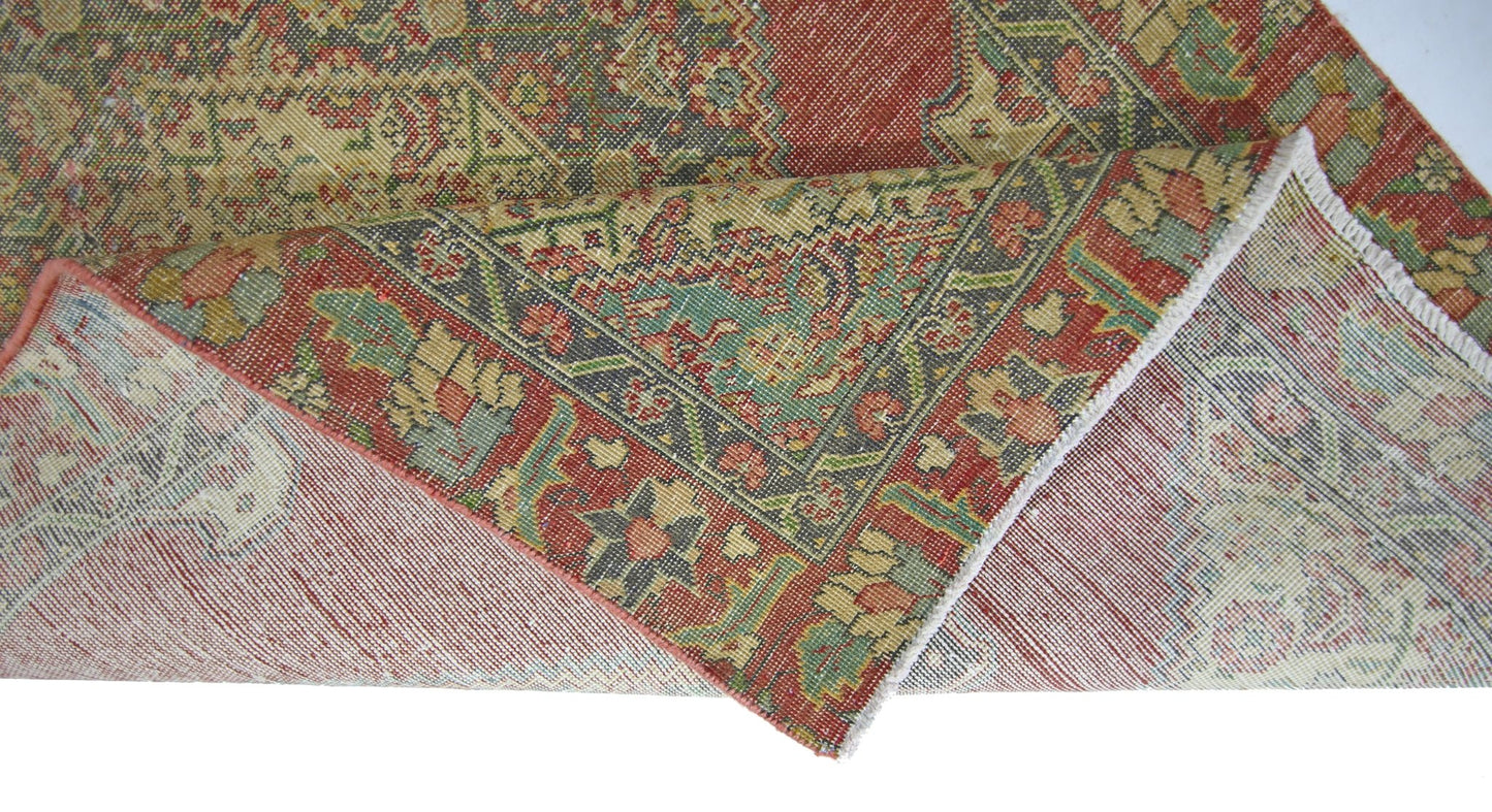 A folded vintage Persian rug featuring intricate floral patterns in red, green, and cream tones.