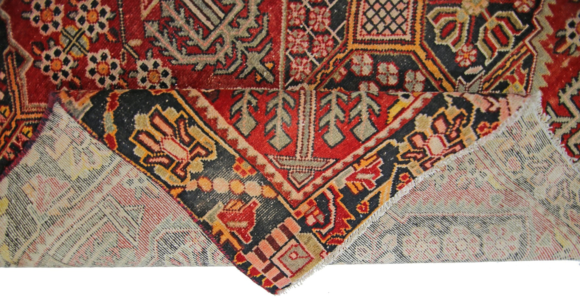 A vintage Persian Tabriz rug with a folded corner showing its intricate red and black pattern.